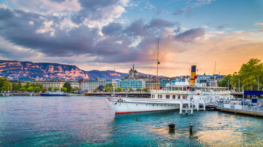 Panoramic view of the historic city center of Geneva with traditional paddle steamer boat on Lake Geneva in beautiful golden evening light at sunset with blue sky and clouds in summer, Switzerland.